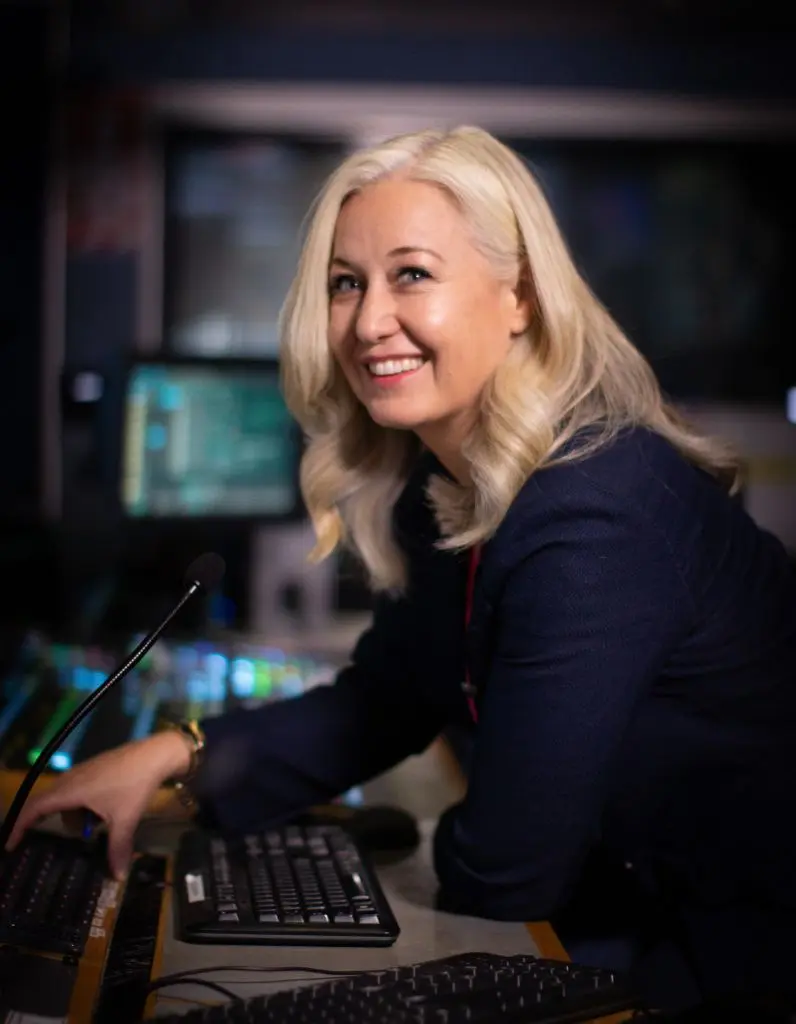 Erica Wood smiling in a newsroom control room in Auckland, reflecting her experience and approachable style as a media training expert.