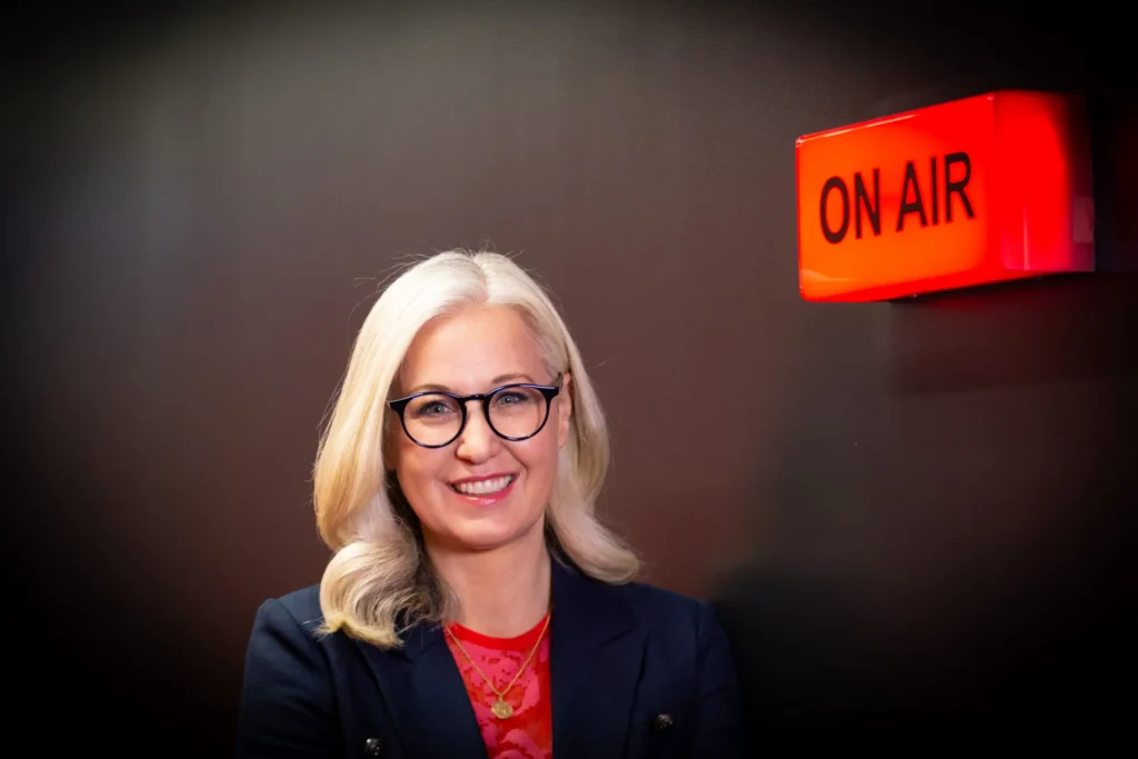 Erica Wood in a media studio beside an ‘On Air’ light, offering professional media training to help clients speak confidently on camera.