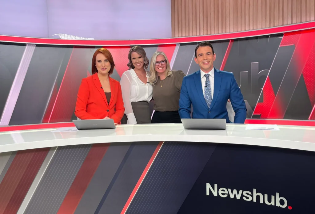 Erica Wood standing with Newshub presenters in the TV studio, reflecting her 20 years of newsroom and media experience.