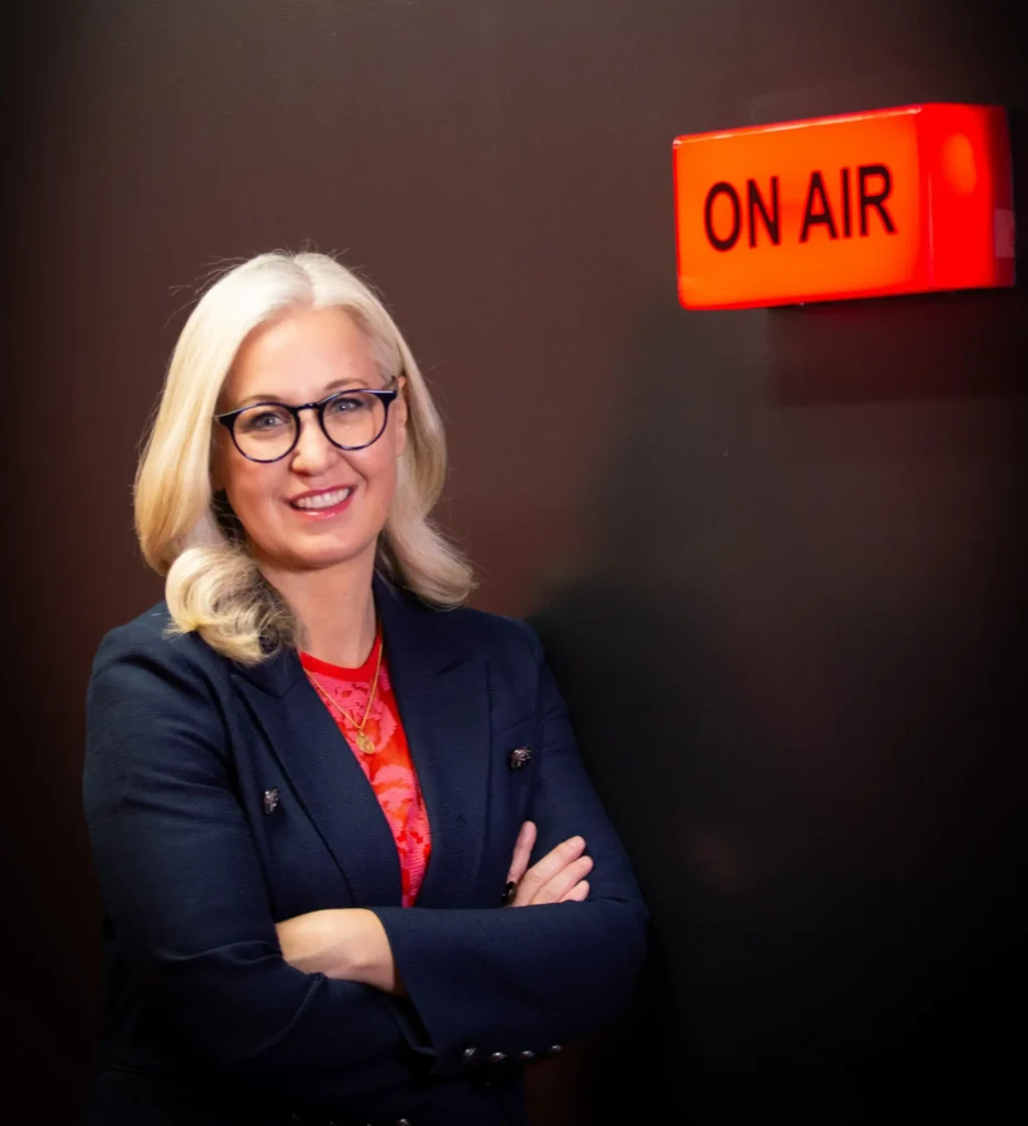 Erica Wood standing beside an illuminated “On Air” sign, representing her broadcast media expertise and media training experience.