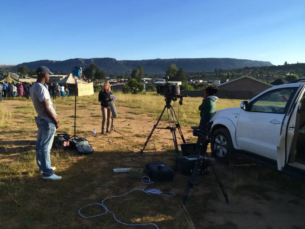 Erica Wood reporting on location with a film crew in a Lesotho field setting, capturing a live news story.